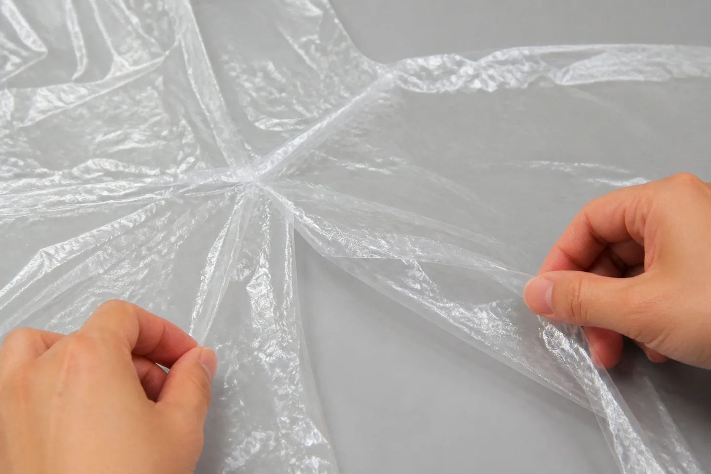 Hands gently separating clear PE poncho layers while reviewing welded edges and an opening