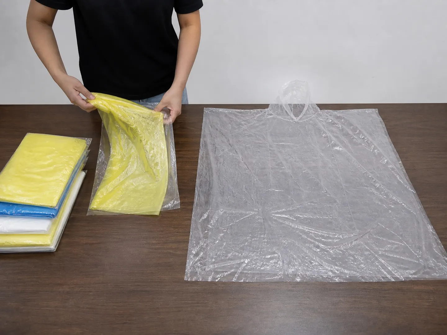 Buyer unfolding a yellow PE poncho pack beside an opened clear cape on a sample table