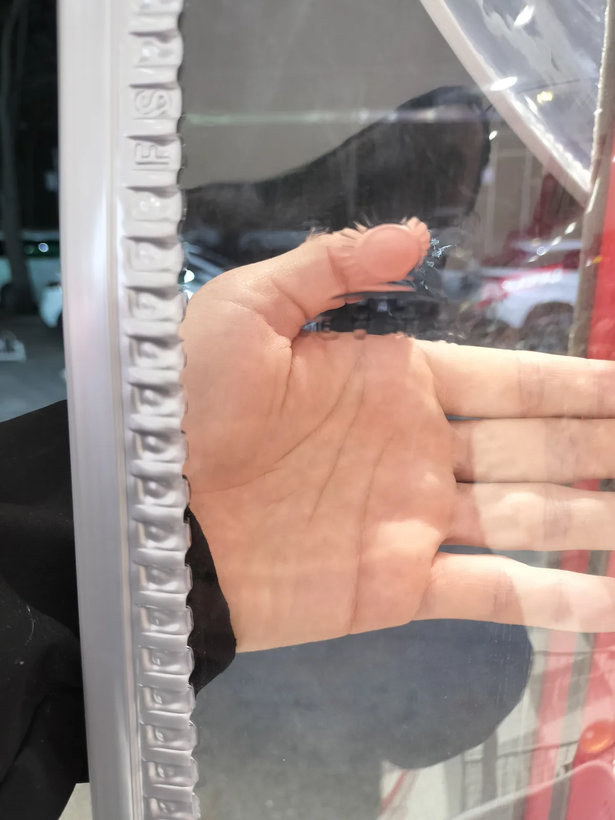 Hand positioned behind a clear panel beside its ribbed gray edge carrier during visual inspection.
