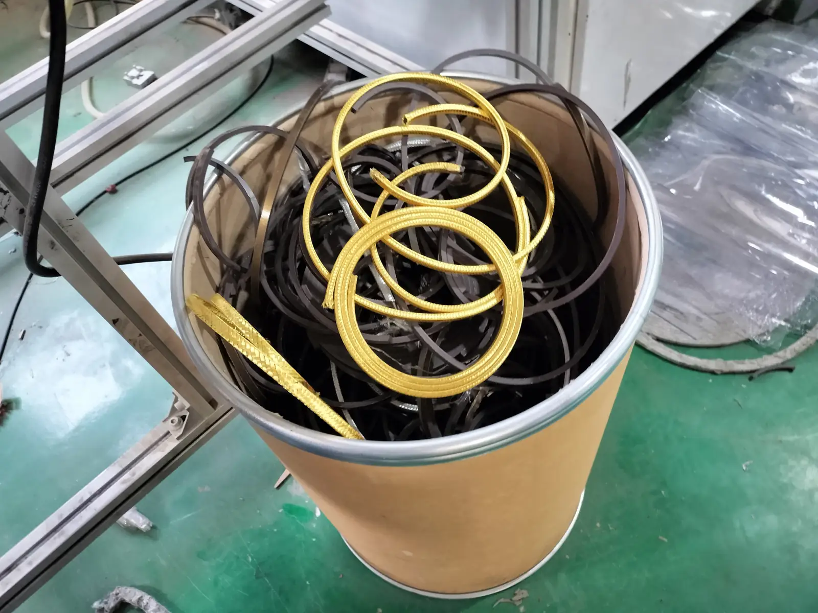 Mixed gray, black and yellow edge-carrier coils staged together inside a plain open drum.