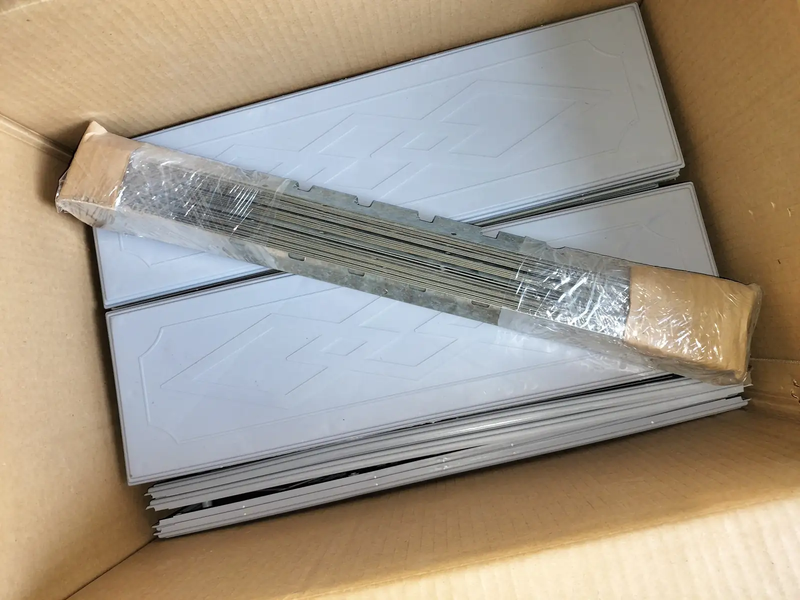 Transparent panel stack and wrapped rail components arranged in a plain shipping carton.
